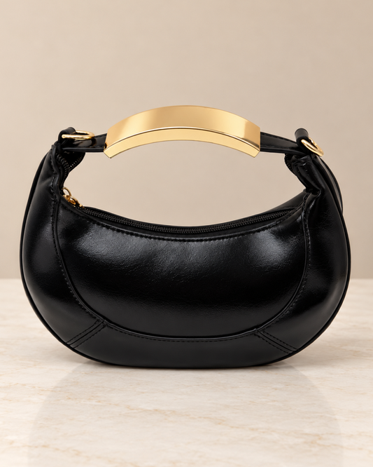 Bolso de fiesta negro brillante con forma de media luna, cierre de cremallera y asa metálica dorada sobre fondo beige.