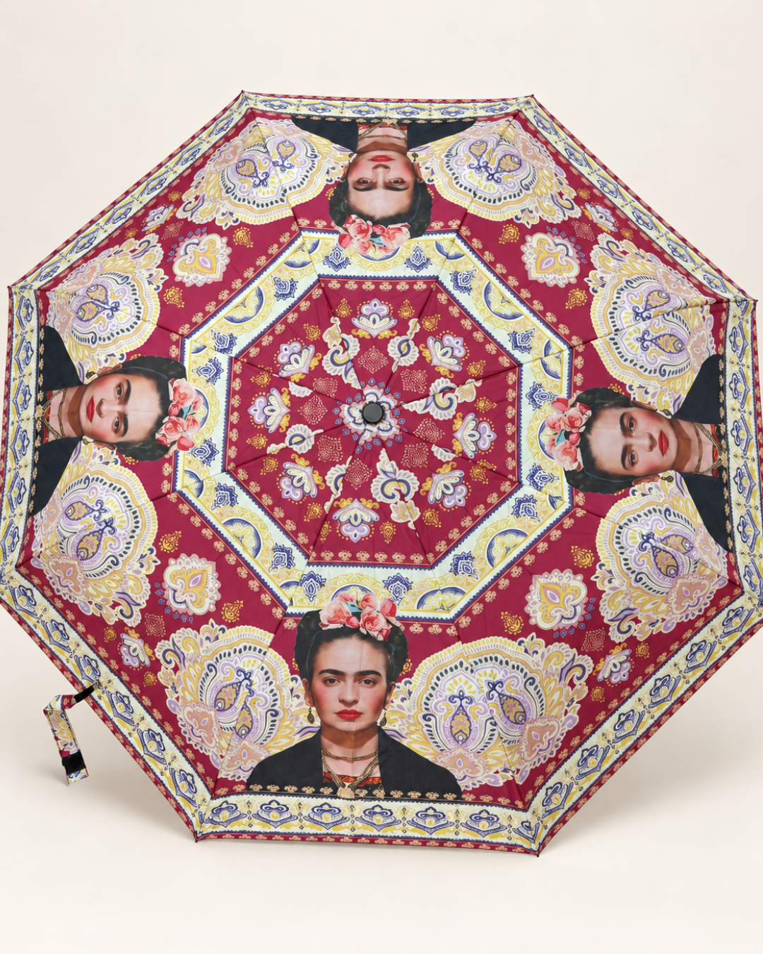 Paraguas Frida Kahlo abierto de perfil con fondo granate, motivos paisley multicolor y mango negro.