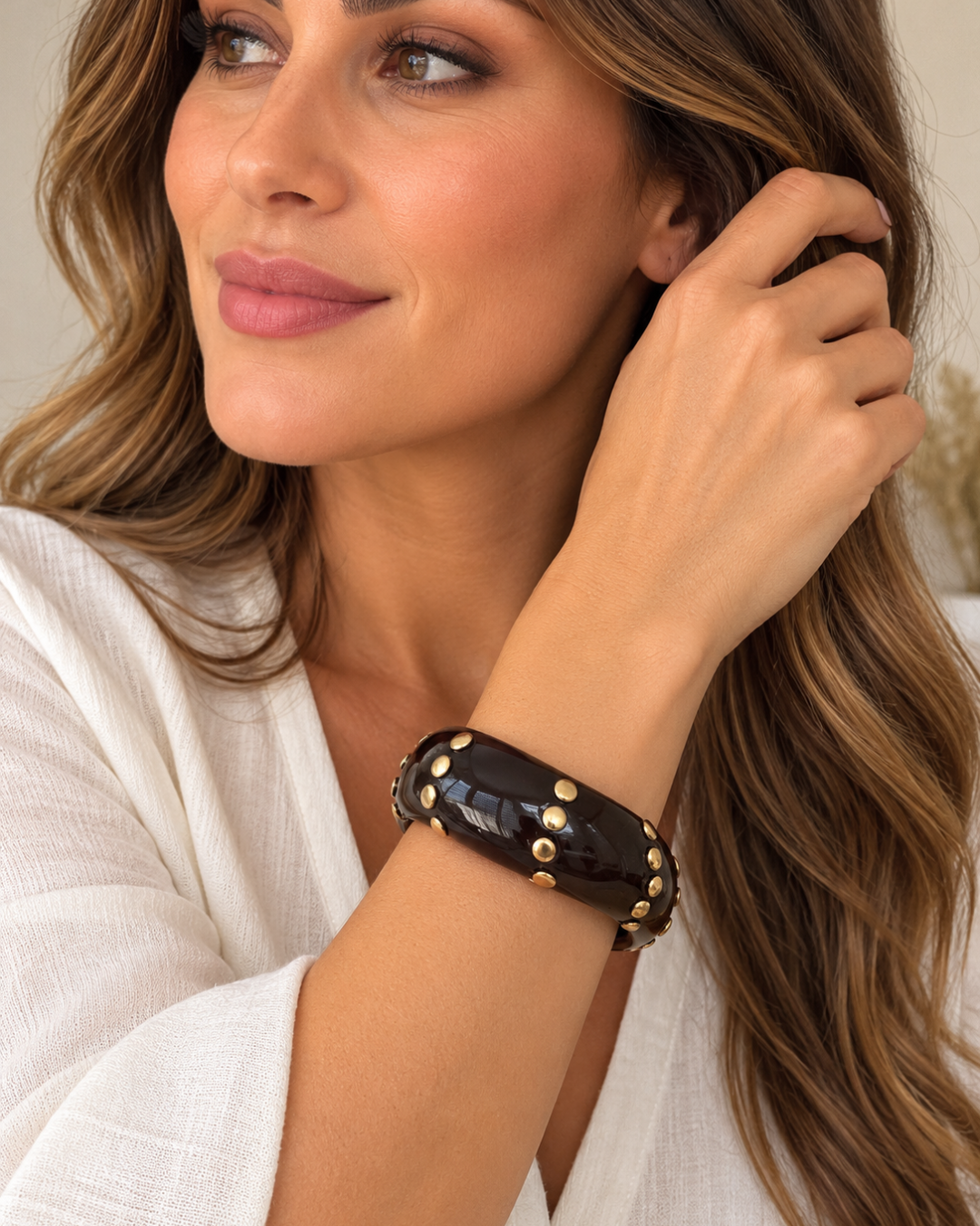 Pulsera brazalete marrón con detalles dorados llevada de forma holgada sobre el antebrazo de una modelo.