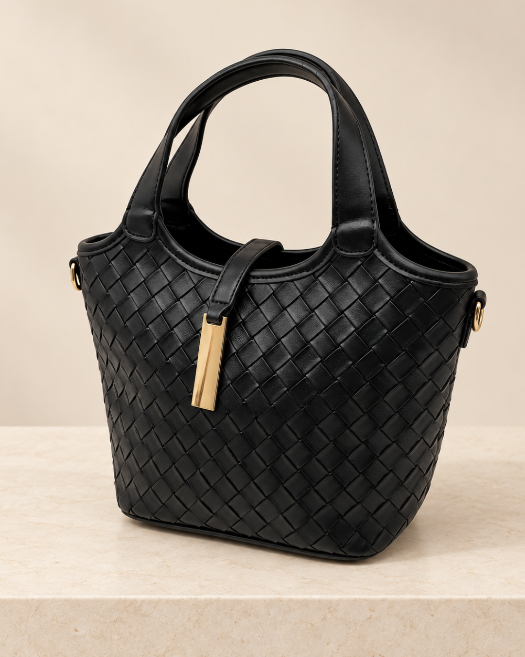 Vista de perfil de bolso negro trenzado con doble asa y detalle metálico dorado sobre fondo beige claro.