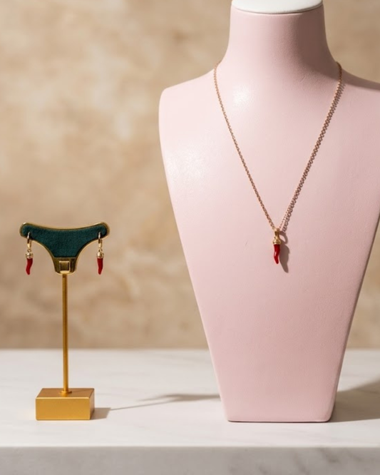 Conjunto de cadena y pendientes corno rosso de acero sobre expositores en un fondo elegante texturizado.