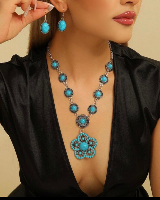 Conjunto de collar con medallón floral turquesa y pendientes a juego puesto en modelo con vestido negro.