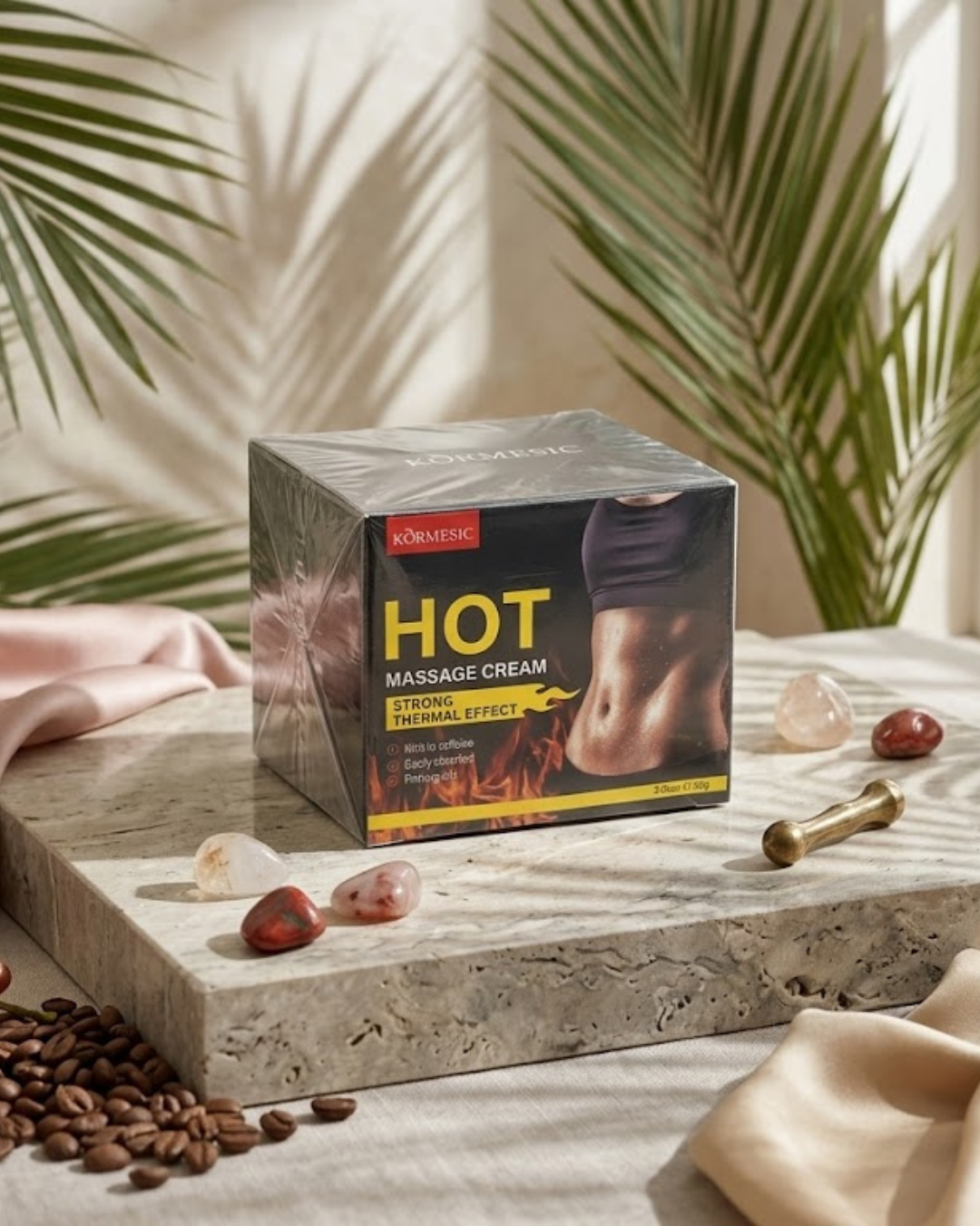 Caja de crema reductora efecto calor KORMESIC Hot Massage Cream 85g rica en cafeína sobre piedra de mármol y granos de café.