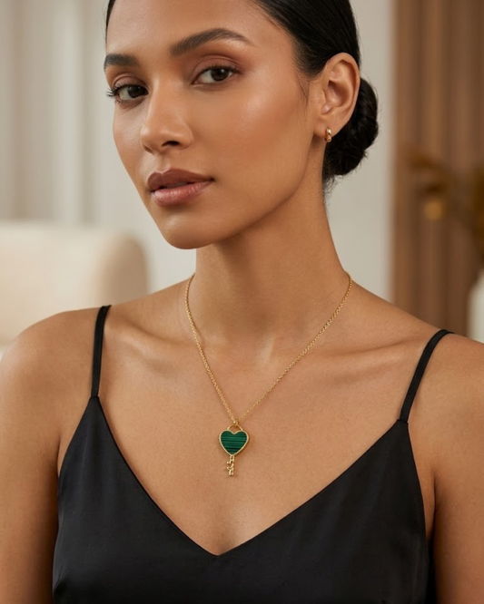 "Mujer con colgante de llave corazón verde y dorado de acero inoxidable sobre vestido negro."