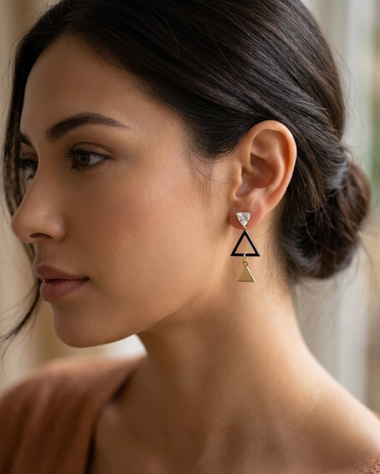 "Pendientes cortos de mujer con diseño de tres triángulos en color oro, negro y cristal, puestos en modelo."