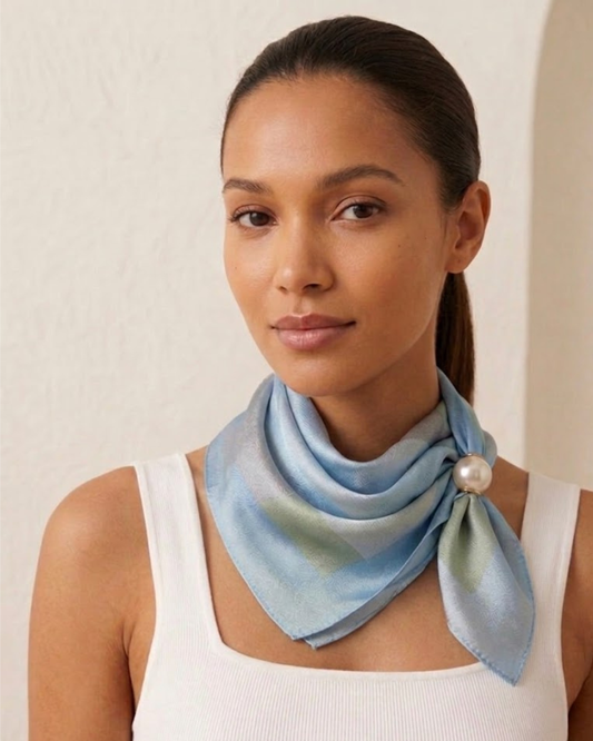 Modelo con pelo recogido luciendo pañuelo azul de tela sedosa con broche de perla premium y camiseta blanca de tirantes.