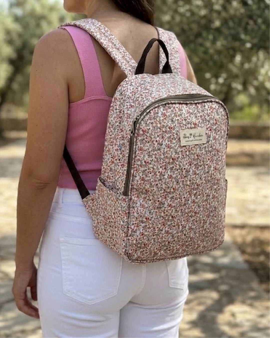 Chica de espaldas con top rosa y pantalon blanco llevando la mochila nevera termica de mini flores Bags Garden en tienda Narella