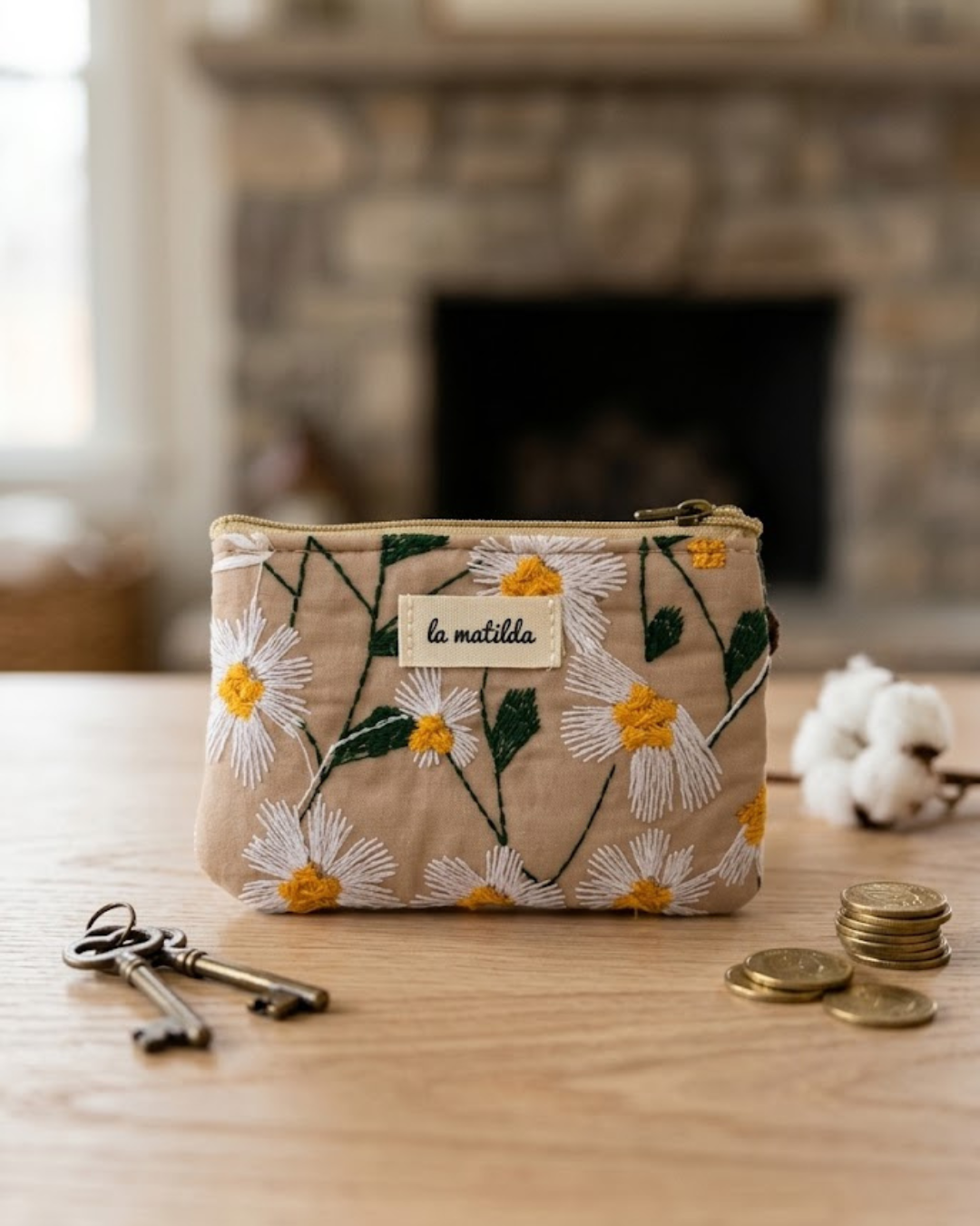 Monedero acolchado beige con bordado de margaritas La Matilda junto a llaves y monedas