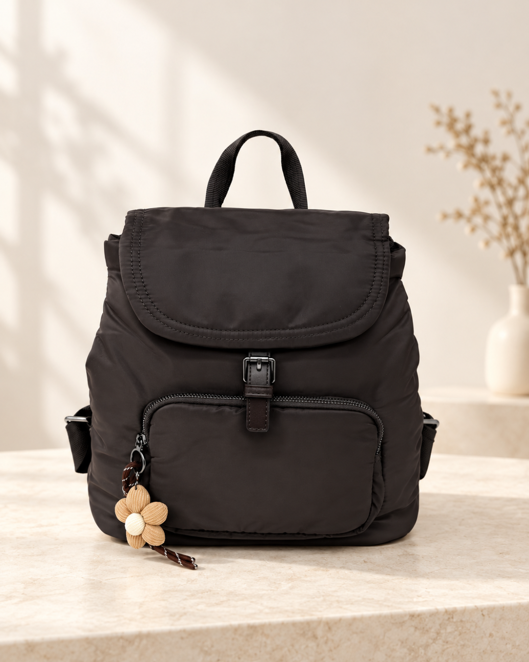 Mochila negra de mujer ligera con bolsillo delantero, solapa y colgante floral