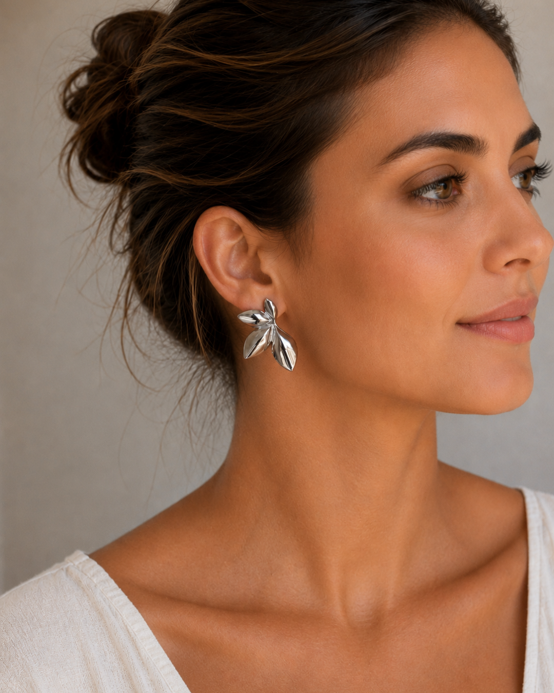 Modelo luciendo pendientes de acero plateado con forma de hojas orgánicas de Accesoriomanía con recogido de pelo.