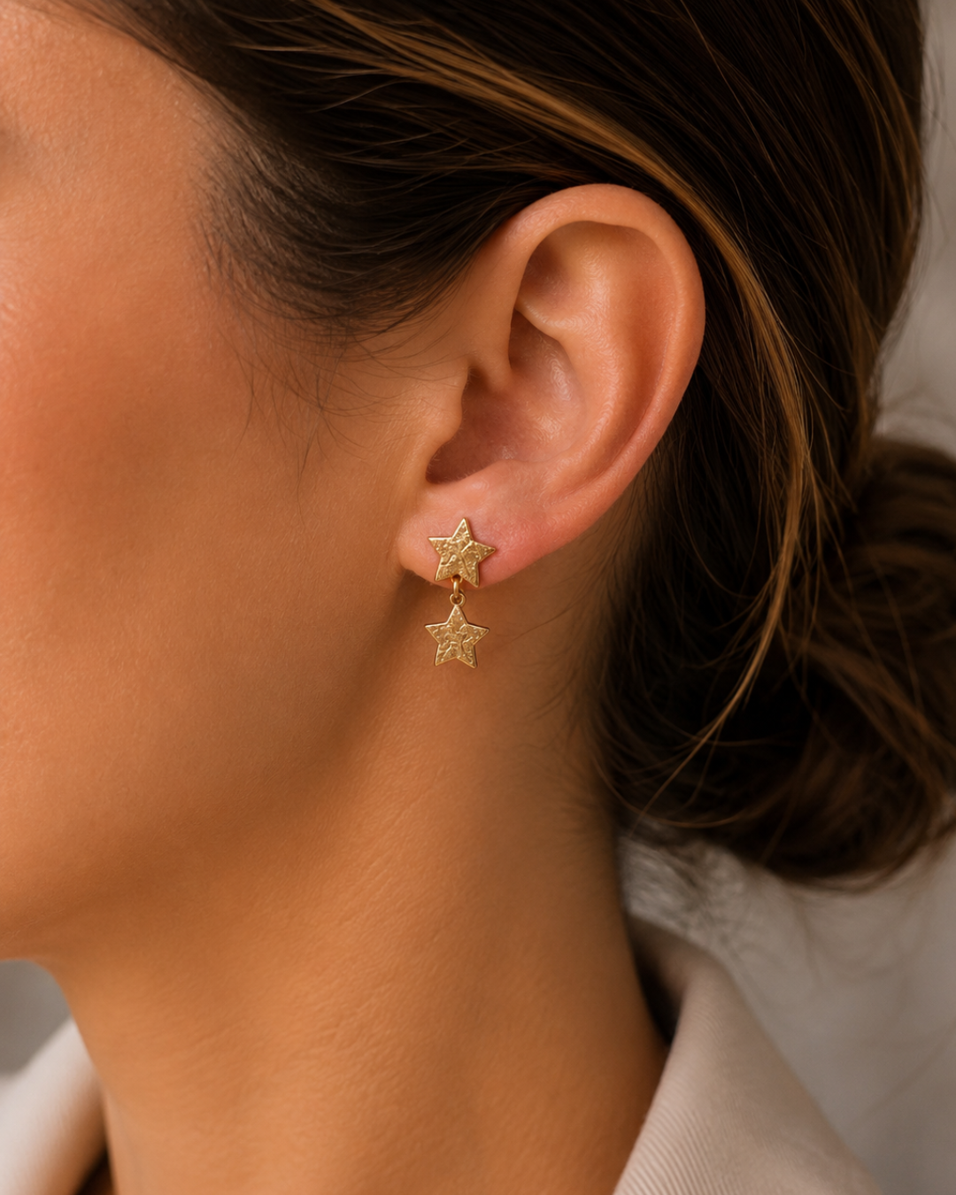 Mujer luciendo pendientes de doble estrella en acero inoxidable dorado con textura