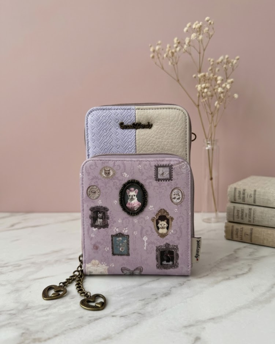 Bolso portamóvil Sweet Candy color lila y malva con marco metálico de perrito, billetero y cremalleras sobre mesa de mármol.