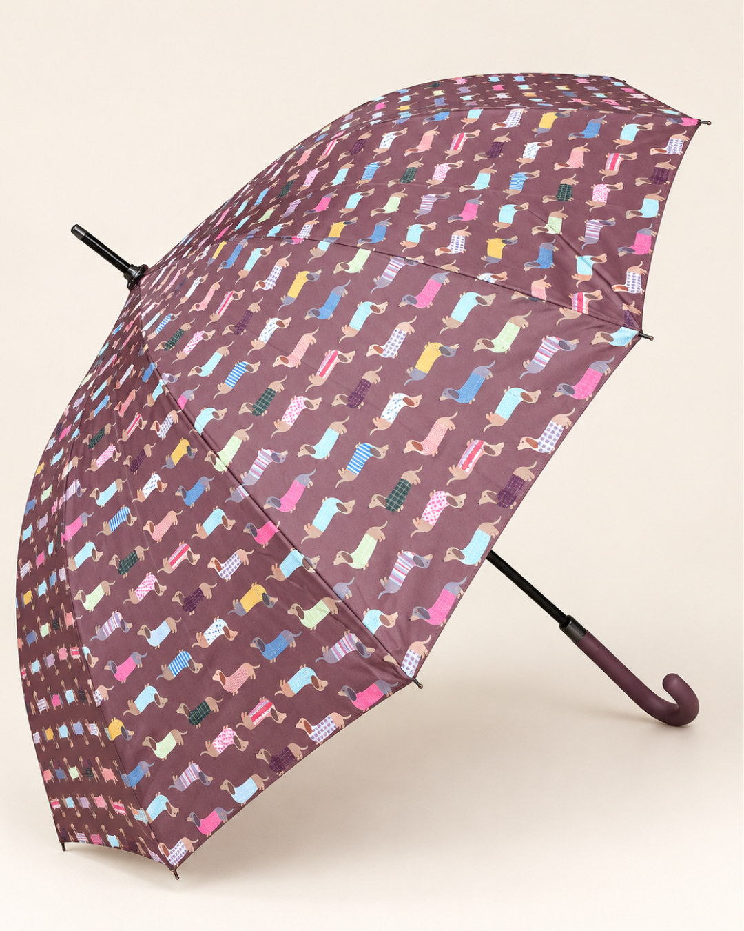 Paraguas de perritos salchicha abierto de perfil, con fondo malva, estampado multicolor y mango curvo a juego.