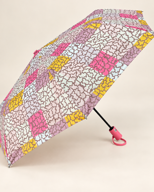 Paraguas plegable abierto con estampado abstracto en tonos rosa, lila y crema, detalles fucsias y amarillos y mango rosa.