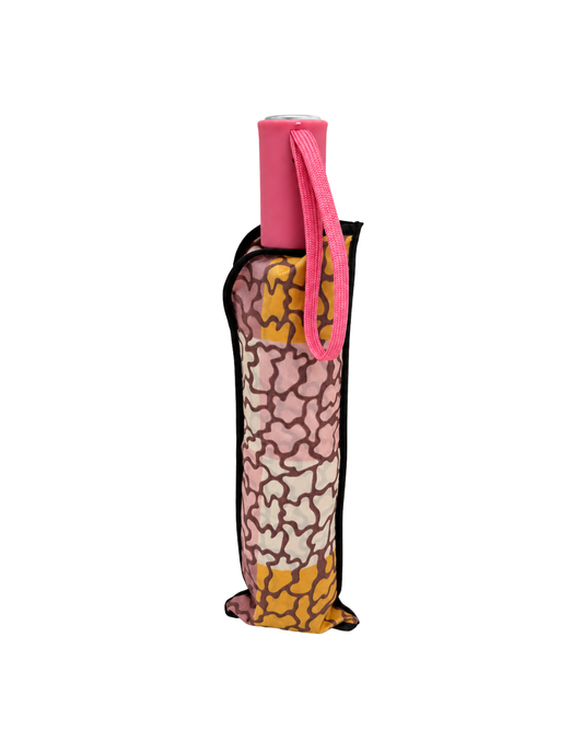 Paraguas plegable cerrado en su funda de estampado abstracto multicolor, con mango rosa y cinta de muñeca.