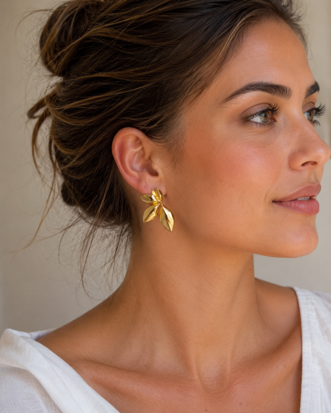 Modelo luciendo pendientes de acero dorado con forma de hojas orgánicas de Accesoriomanía con recogido de pelo.