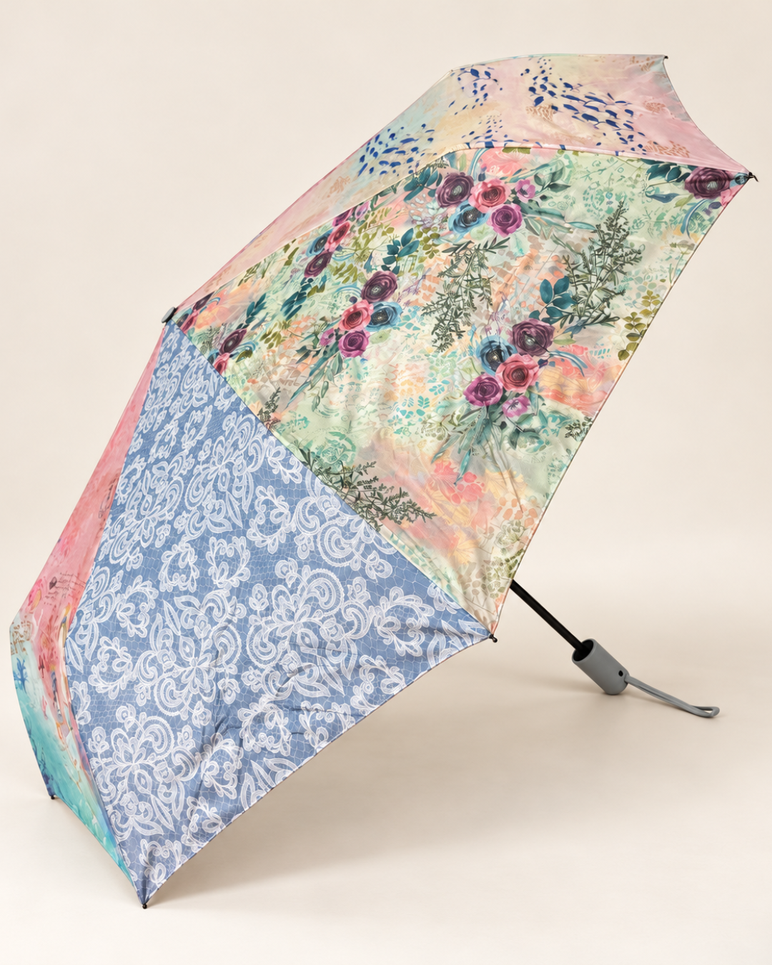 Vista lateral de paraguas plegable Sweet Candy con estampado floral rosa y verde, motivos ornamentales azules y mango gris con cinta para la muñeca.