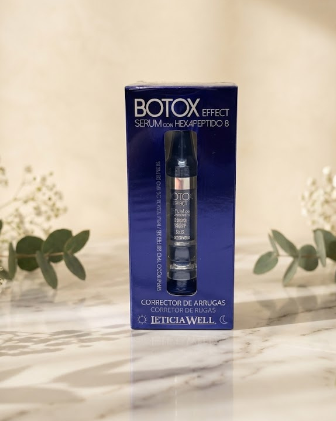 Caja azul de sérum corrector de arrugas Leticia Well Botox Effect con Hexapéptido-8 sobre fondo de mármol con flores frescas.