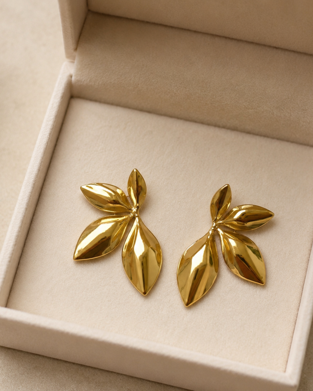 Pendientes de acero inoxidable dorado con diseño de hojas pulidas sobre estuche beige de Accesoriomanía.