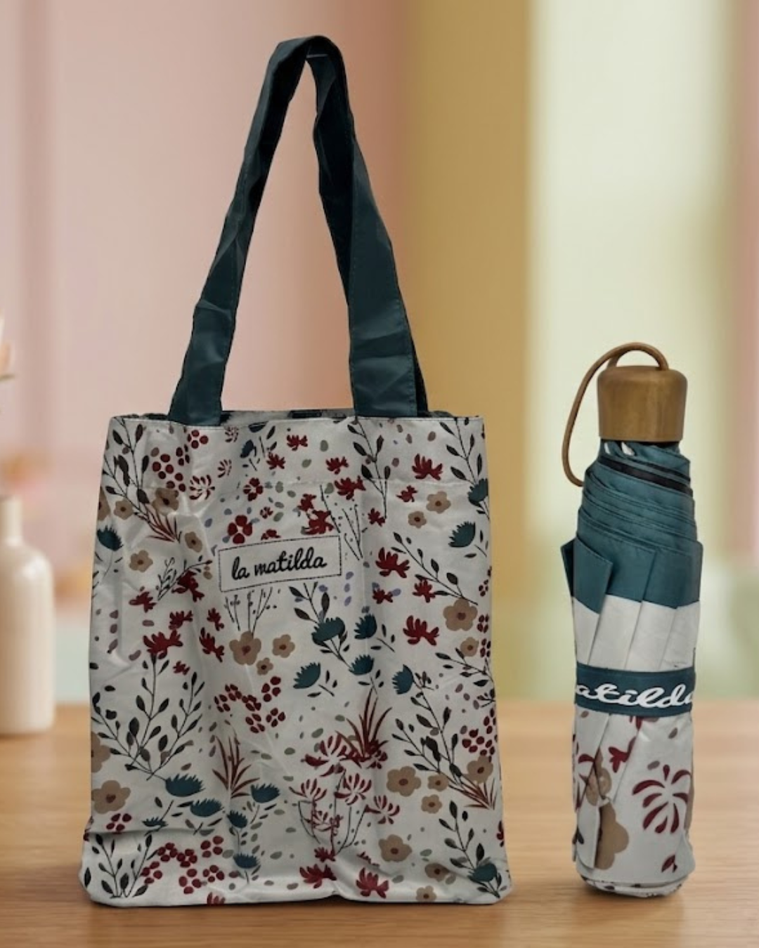 Set de paraguas plegable automático y bolsa de tela a juego con estampado floral botánico de La Matilda sobre mesa de madera clara