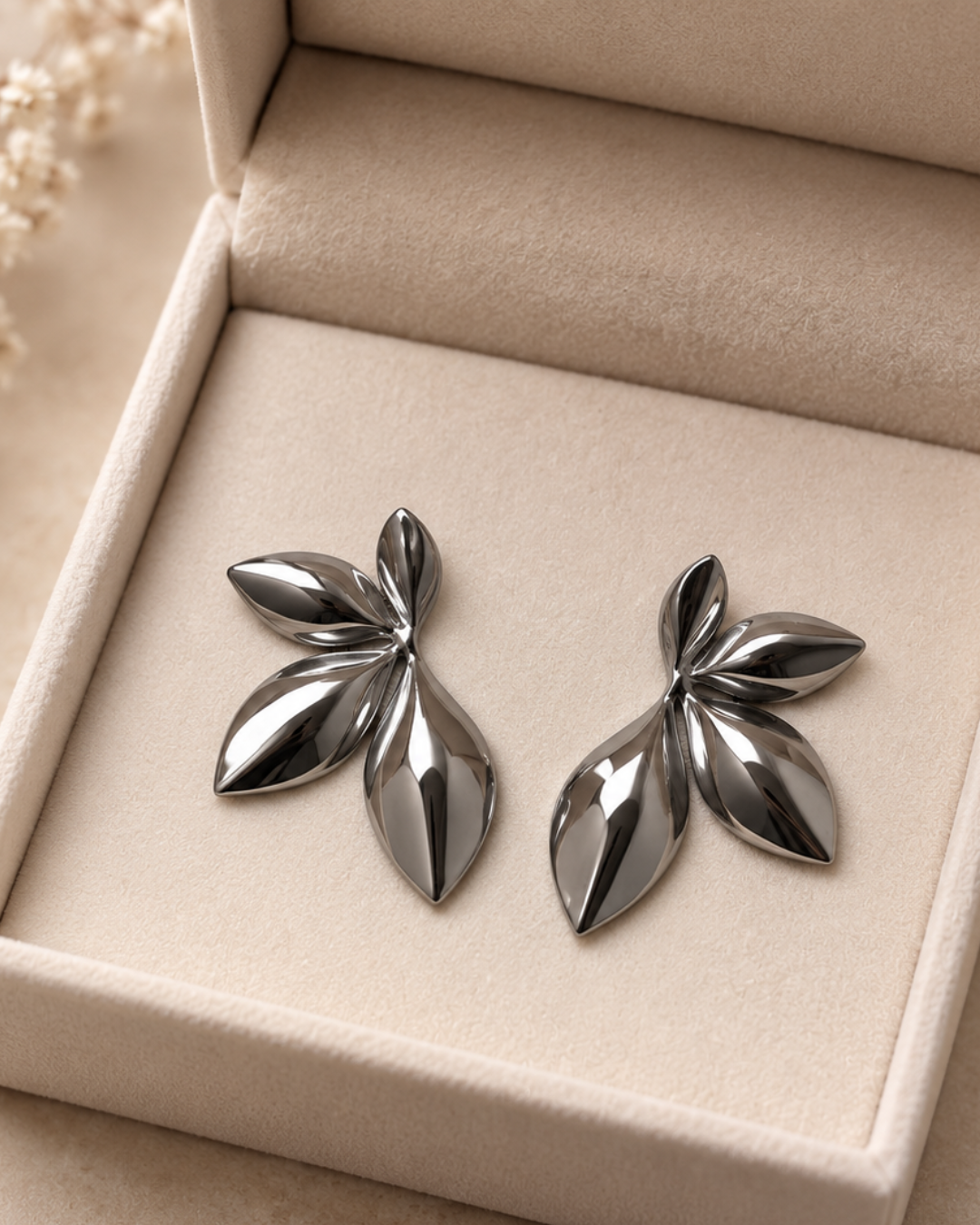 Pendientes de acero inoxidable plateado con diseño de hojas pulidas sobre estuche beige de Accesoriomanía.